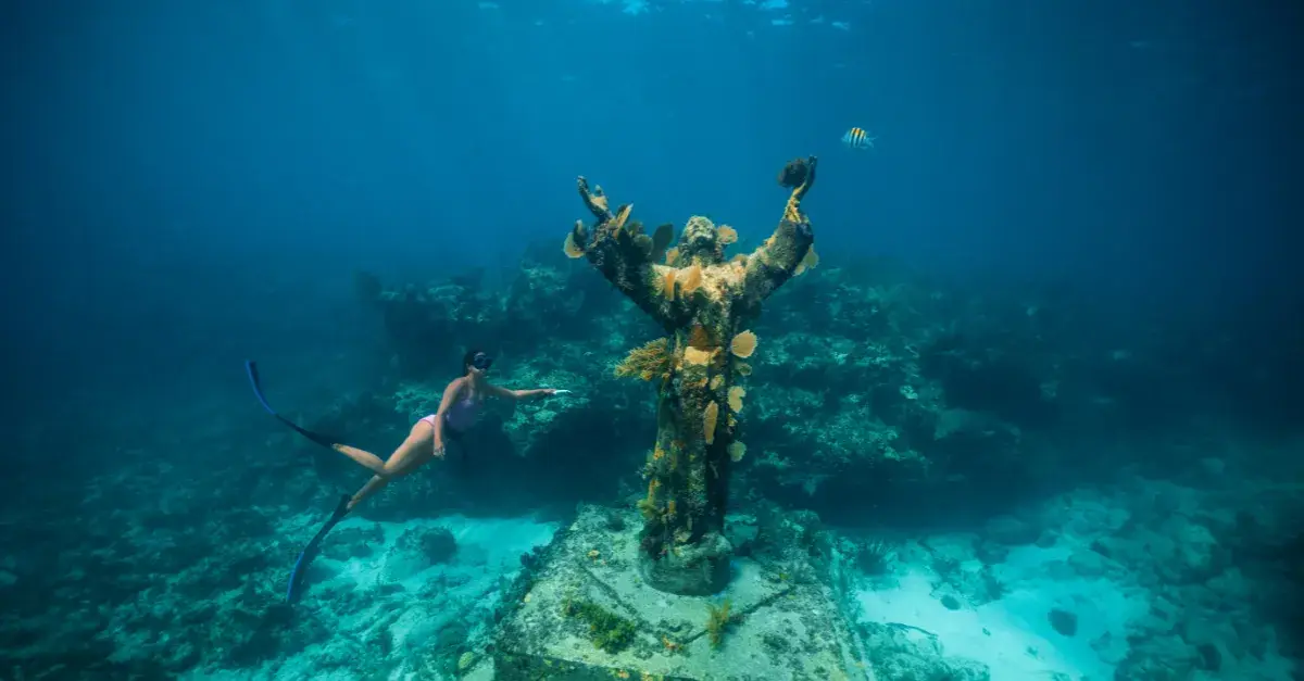 Freediver swimming beside the Christ of the Abyss statue
